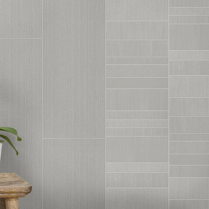 Modern gray tile wall with different textures, wooden stool, and green houseplant on light gray flooring