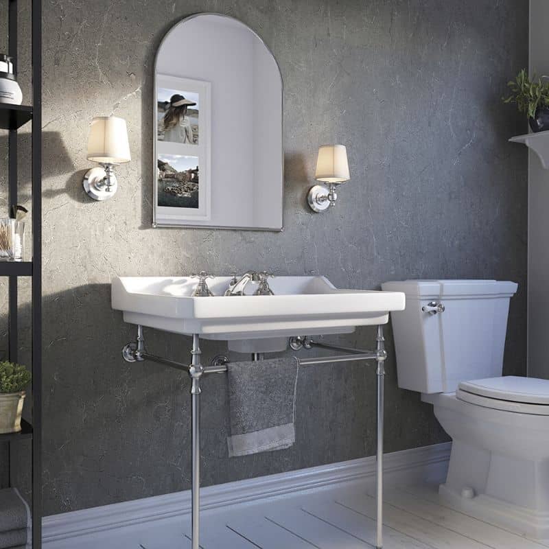 Modern bathroom interior with wall-mounted sink, chrome fixtures, arched mirror, wall sconces, toilet, grey textured walls, and white wooden flooring.