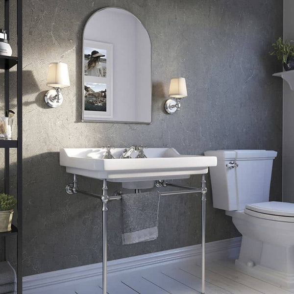 Modern bathroom interior with wall-mounted sink, chrome fixtures, arched mirror, wall sconces, toilet, grey textured walls, and white wooden flooring.